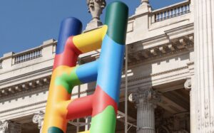 A 20-meter rainbow-colored ladder installation by Paola Pivi leans against the Grand Palais Éphémère in Paris, 2025